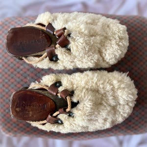 Puede incluir: Un par de zapatillas blancas y peludas con suelas de cuero marrón y cordones. Las zapatillas tienen la palabra "ECCO" escrita en las suelas.