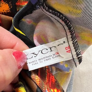 以下が含まれることがあります： 黒い文字で「Lycra Marca Registrada de DuPont Para Su Fibra Elasto」と書かれた白いタグのクローズアップ。黒い星と数字の42がタグに印刷されています。