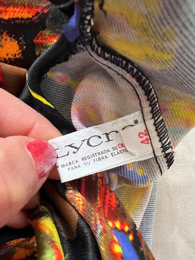 以下が含まれることがあります： 黒い文字で「Lycra Marca Registrada de DuPont Para Su Fibra Elasto」と書かれた白いタグのクローズアップ。黒い星と数字の42がタグに印刷されています。