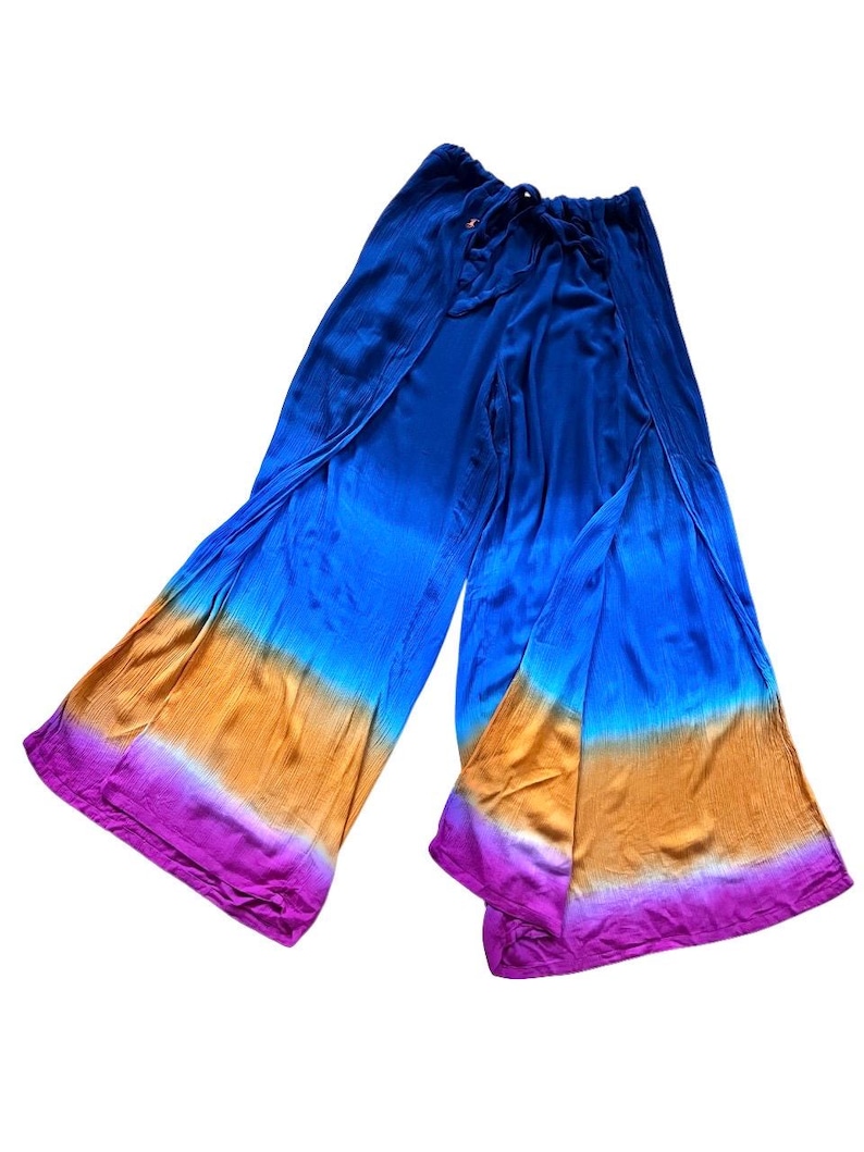 May include: Blue, orange, and purple tie-dye palazzo pants. The wide-leg pants have a drawstring waist and a split design. The fabric has a textured appearance and a gradient color scheme, transitioning from blue to orange and purple.
