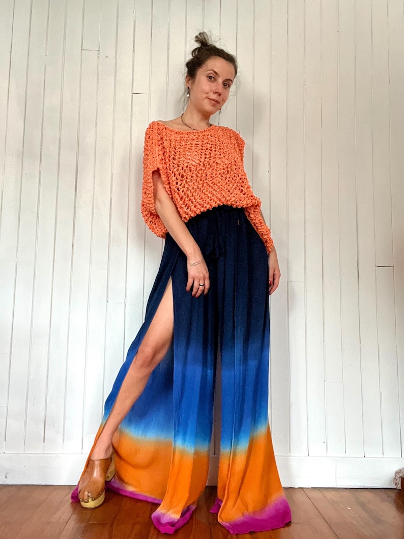 May include: An orange crochet top paired with navy blue and ombre blue-orange palazzo pants. The pants have a high slit on the side. The outfit is worn with wooden clogs.