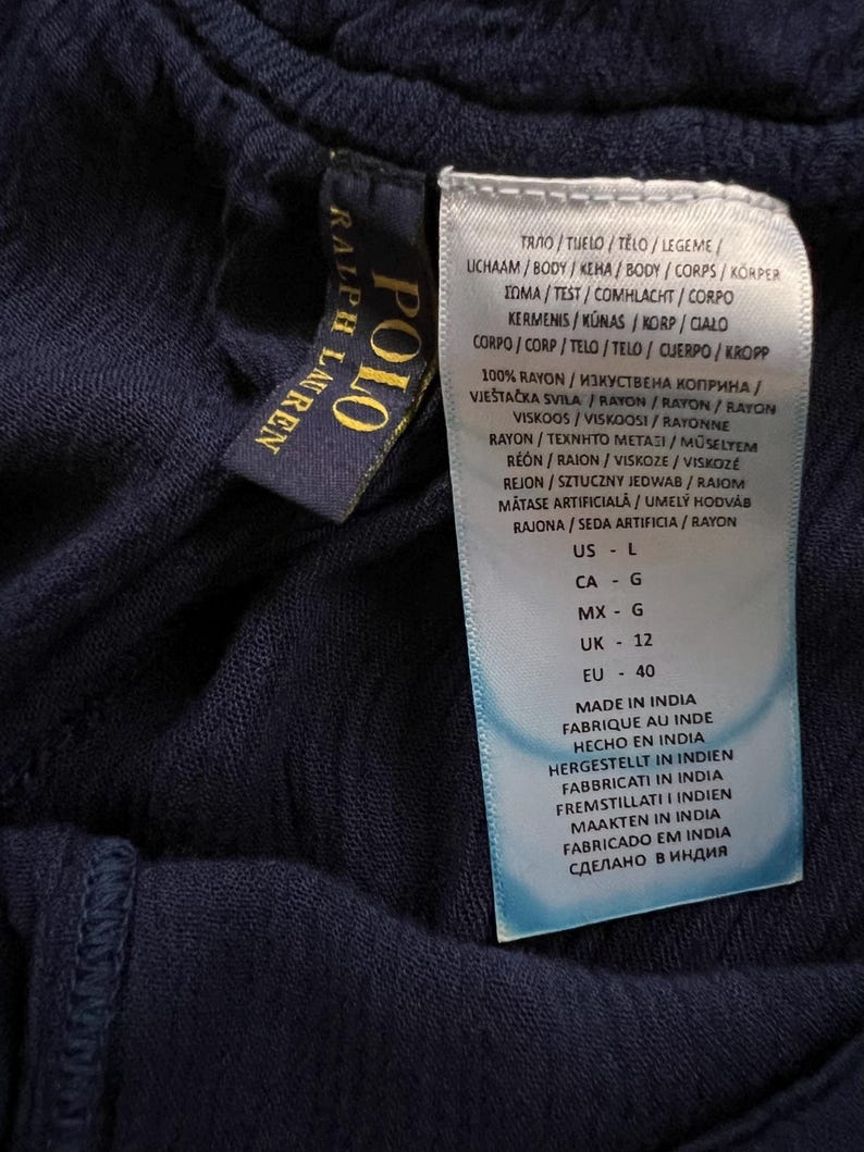 May include: Navy blue fabric with two tags. One tag reads "POLO RALPH LAUREN" in gold lettering on a navy blue background. The other tag has white text on a white background, with information about the fabric content and origin.