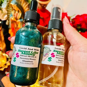 May include: Two glass bottles with black caps and labels that read "Lucid And Wild Sweet Like Money." One bottle contains a teal liquid, the other a clear liquid. The labels also say "Attract Money & Sweeten Money Situations Body & Ritual Oil."