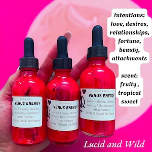 May include: Three bright pink glass bottles with black droppers are labeled "Venus Energy." The labels list intentions: love, desires, relationships, fortune, beauty, and attachments. The scent is described as fruity, tropical, and sweet. The brand name "Lucid and Wild" is also visible.