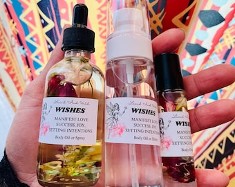 Puede incluir: Tres frascos de vidrio transparente con aceite corporal botánico y spray. Las etiquetas dicen Lucid And Wild WISHES MANIFEST LOVE SUCCESS, JOY, SETTING INTENTIONS Body Oil or Spray, con una ilustración de hada y detalles florales rosas.