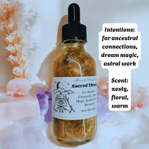 May include: A clear glass bottle with a black dropper top, filled with a golden-brown liquid. The label reads "Sacred Thread" with text about ancestral connection, dream magic, and astral work. The scent is described as zesty, floral, and warm.