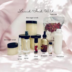 Op de afbeelding: Een verzameling zelfzorgproducten, waaronder suikerscrubs, sprays, rollers, een druppelfles, een flesje, badzout en lotion. De producten zitten in transparante potten en flessen met zwarte deksels en etiketten. De tekst "Lucid And Wild" staat bovenaan.