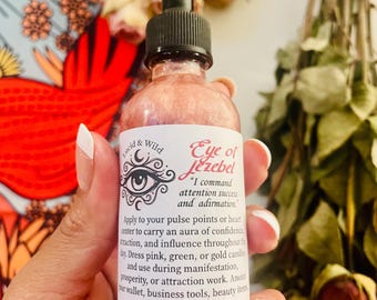 Puede incluir: Un frasco cuentagotas de vidrio transparente lleno de un líquido rosa brillante. La etiqueta blanca presenta un gráfico de ojo negro, el texto Lucid & Wild, Eye of Jezebel, y las instrucciones con la frase I command attention success and admiration.