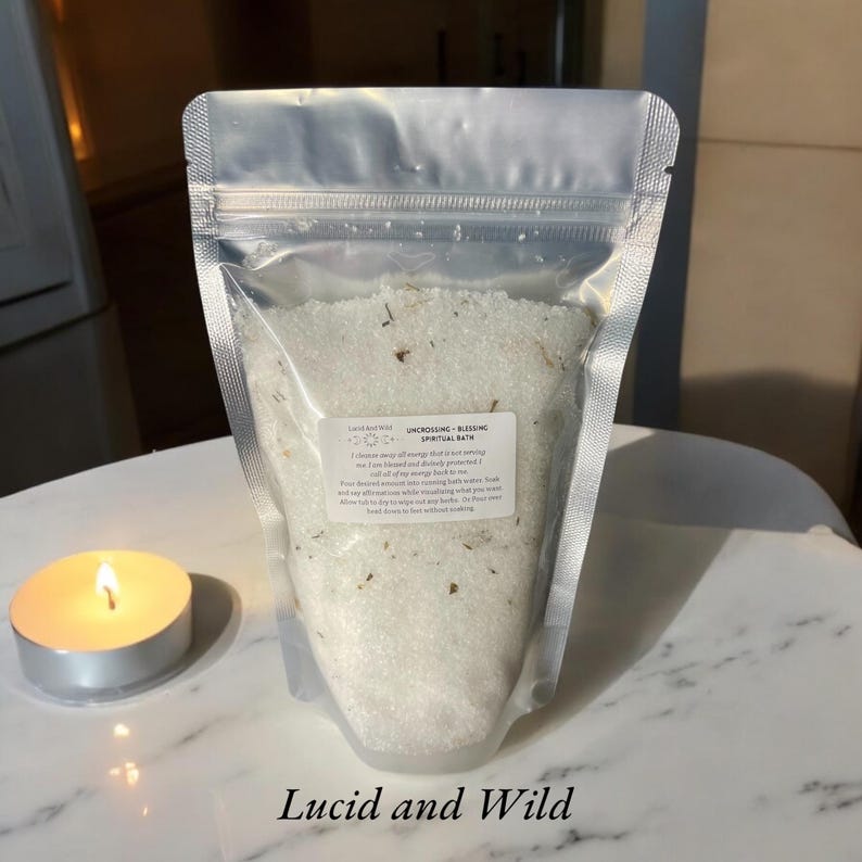 May include: A white resealable pouch filled with white bath salts and dried flowers. The pouch has a label that reads "Unconscious - Blessing Spiritual Bath". The text "Lucid and Wild" is printed below the pouch.