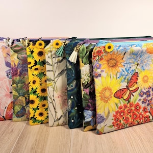 May include: A collection of 10 zippered pouches with various floral and nature-inspired prints. The pouches are made of fabric and have a zipper closure. The prints include sunflowers, butterflies, and other flowers.
