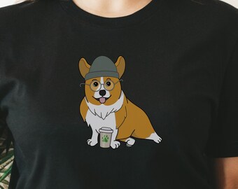 Könnte beinhalten: Ein schwarzes T-Shirt mit einem Cartoon-Bild eines Corgis, der einen Hut und eine Brille trägt und eine Tasse Kaffee hält.