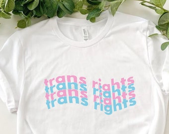 Könnte beinhalten: Weißes T-Shirt mit dem Satz "trans rights" viermal in rosa und blauen Buchstaben wiederholt.