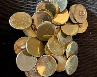 May include: A pile of round, gold-colored buttons with a shiny finish. The buttons have a raised edge and a small hole in the center.