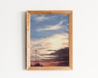 May include: A framed painting of a sunset with a power line in the foreground. The sky is a mix of blue, pink, and orange with dark clouds in the distance. The power line is silhouetted against the sunset.