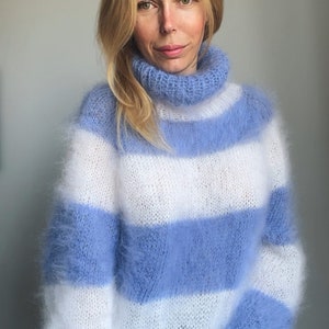 Op de afbeelding: Een blauwe en witte gestreepte, fuzzy gebreide trui met een turtleneck.