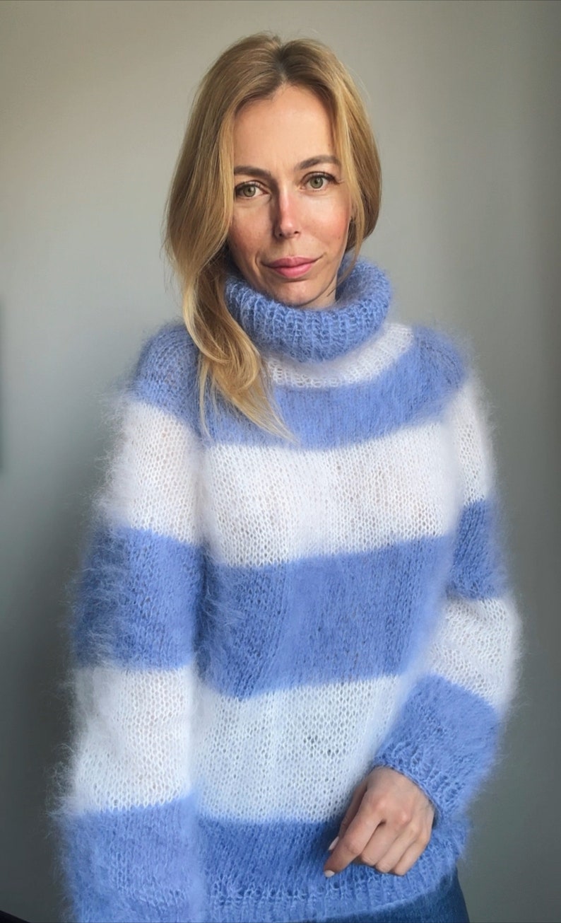 Op de afbeelding: Een blauwe en witte gestreepte, fuzzy gebreide trui met een turtleneck.