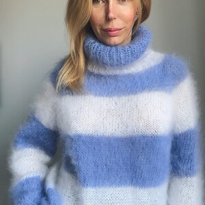 Op de afbeelding: Een blauwe en witte gestreepte, fuzzy trui met een hoge hals. De trui is gemaakt van een zacht, pluche garen en heeft een ontspannen pasvorm.
