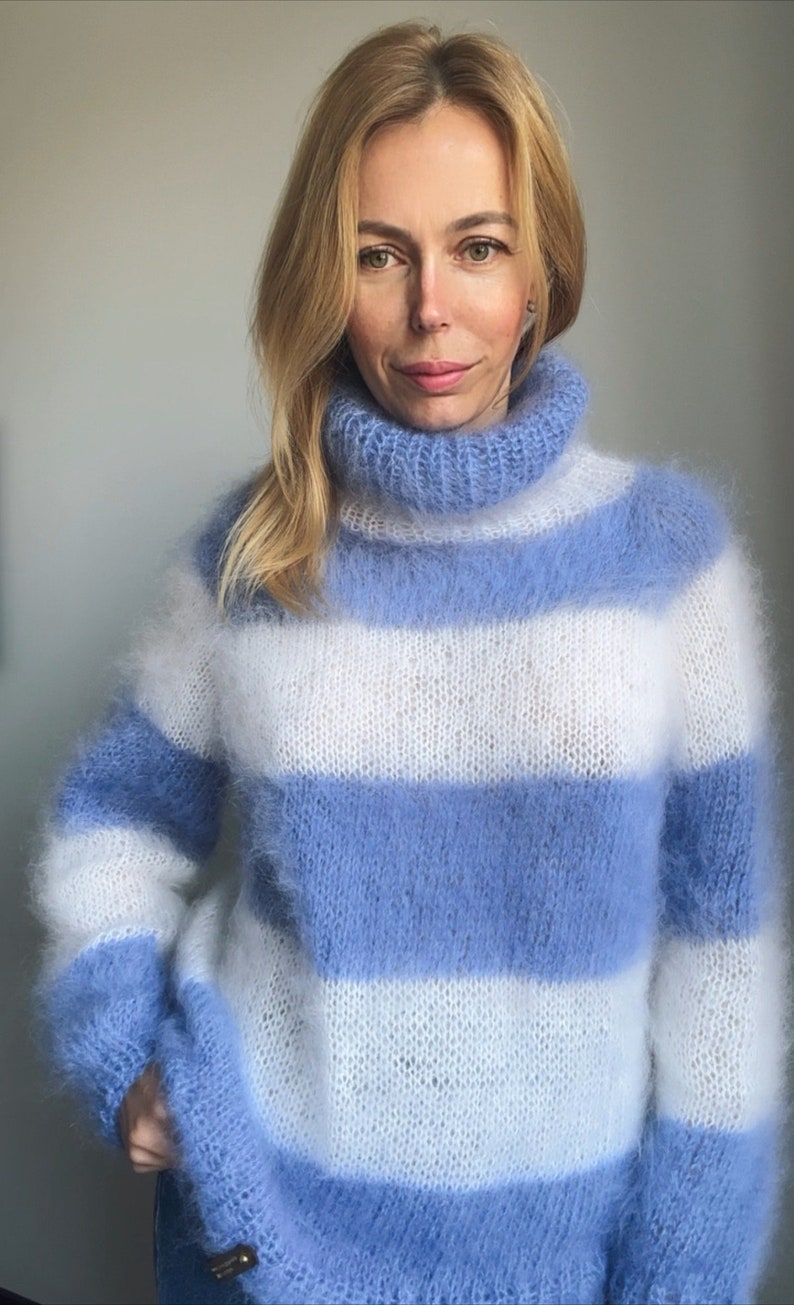 Op de afbeelding: Een blauwe en witte gestreepte, fuzzy trui met een hoge hals. De trui is gemaakt van een zacht, pluche garen en heeft een ontspannen pasvorm.