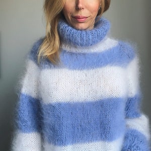 Op de afbeelding: Een blauwe en witte gestreepte, pluche gebreide trui met een hoge hals.