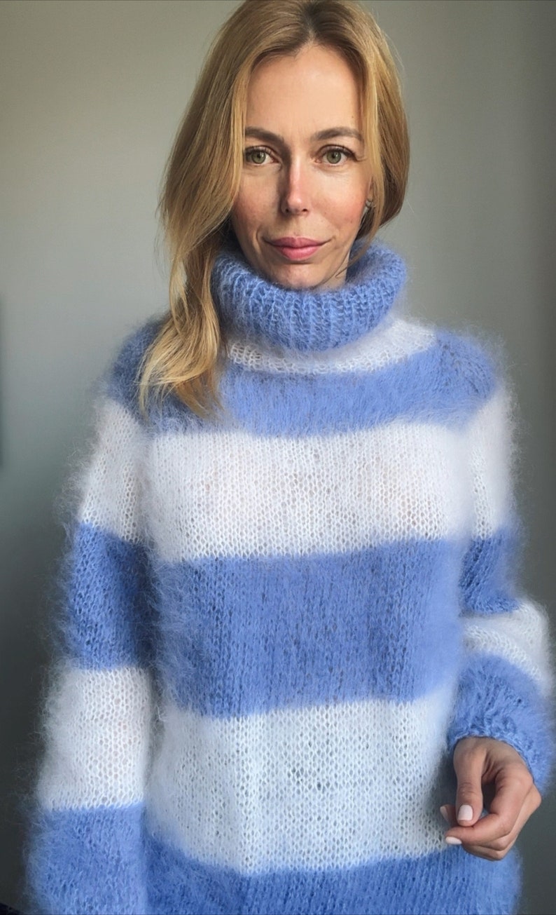 Op de afbeelding: Een blauwe en witte gestreepte, pluche gebreide trui met een hoge hals.
