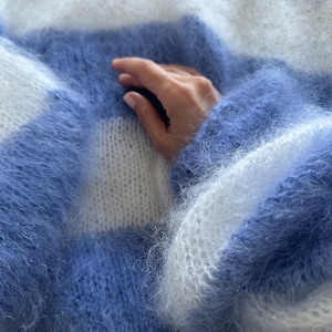 Op de afbeelding: Een zachte, pluche blauwe en witte gestreepte trui met een hand die op de stof rust.