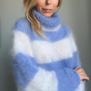 Op de afbeelding: Een blauwe en witte gestreepte, fuzzy gebreide trui met een hoge hals.