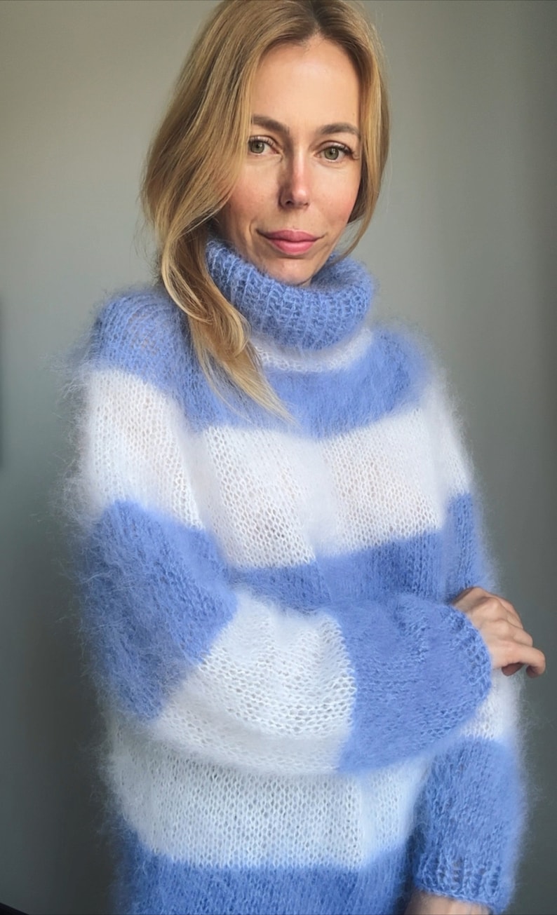 Op de afbeelding: Een blauwe en witte gestreepte, fuzzy gebreide trui met een hoge hals.