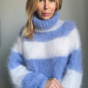 Op de afbeelding: Een blauwe en witte gestreepte, pluche gebreide trui met een rolkraag.