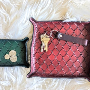 May include: Two leather catchall trays with a scale pattern. The larger tray is red and has a key chain with keys inside. The smaller tray is green and has three coins inside.