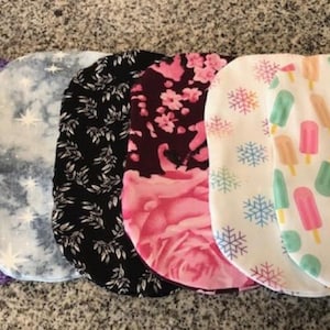 May include: Eight fabric burp cloths in various patterns, including pink floral, purple floral, blue tie-dye, black and white, pink and white floral, white with snowflakes, white with popsicles, and green with brown dots.