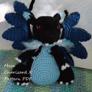 May include: A crocheted plush toy of Mega Charizard X, a Pokemon character. The toy is black and blue with red eyes. The toy is sitting on a green and blue patterned surface. The text "Mega Charizard X Pattern PDF" is visible in the image.