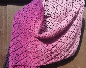 May include: A crocheted shawl in a gradient of pink and purple colors. The shawl is made with a delicate open stitch pattern.