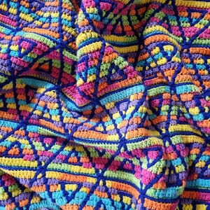 Puede incluir: Una vibrante manta de ganchillo hecha a mano con un patrón geométrico de triángulos en un espectro de colores que incluye azul, rosa, naranja, amarillo y verde. La manta está hecha con hilo suave y tiene una superficie texturizada.