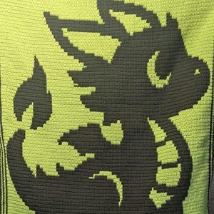 May include: A handmade crochet blanket with a dark grey dragon design on a bright green background. The dragon is stylized with a flame detail. The blanket is square and has a dark green border.