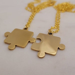 May include: Two gold necklaces with puzzle piece pendants that fit together. The necklaces are made of a delicate chain.