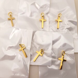 May include: Six gold-colored cross charms packaged in individual clear plastic bags. The charms are simple, with a plain cross design.