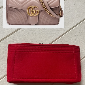 May include: A dusty rose-colored, quilted leather handbag with a gold chain strap and a prominent gold double-G logo. The bag features a flap closure and a structured design. A bright red felt organizer is also shown.