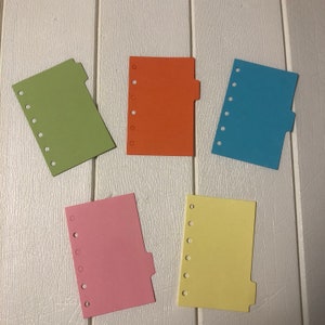 May include: Five colorful index cards with rounded corners and punched holes along the left edge. Each card has a tab on the right side. The colors are green, orange, blue, pink, and yellow.