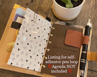 May include: A brown leather bound Louis Vuitton agenda with a self-adhesive pen loop. The text "TODAY" is visible on a tab. The text "LOUIS VUITTON AGENDA 2003 DIARY" is visible on the cover. The text "Listing for self-adhesive pen loop !! Agenda NOT included !!" is visible on the cover.