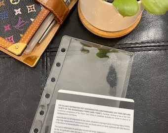 May include: A clear plastic card holder with a black and white card inside. The card has the text "FOR BALANCE INFORMATION VISIT DAVEANDBUSTERS.COM/POWERCARD, SAVE YOUR CHIPS AND TICKETS ON THIS RECHARGEABLE POWER CARD ("CARD")" and the numbers "170427321" and "1856".