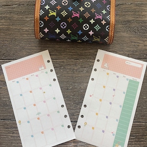 May include: Two pages of a pastel colored planner with a grid pattern and a monthly calendar. The planner has a pink, green, and white color scheme with a small illustration of a rabbit on the left page and a cat on the right page. The planner has a section for notes and a section for each day of the week.