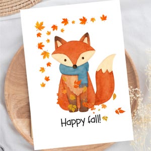 May include: A white greeting card featuring a watercolor illustration of a fox with a blue scarf, surrounded by scattered orange and yellow autumn leaves. The text Happy fall! is printed in black at the bottom of the card design.