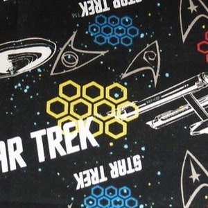 K&ouml;nnte beinhalten: Schwarzer Stoff mit einem sich wiederholenden Muster aus dem Star Trek-Logo, Sternen und Wabenformen in Gelb, Rot und Blau.