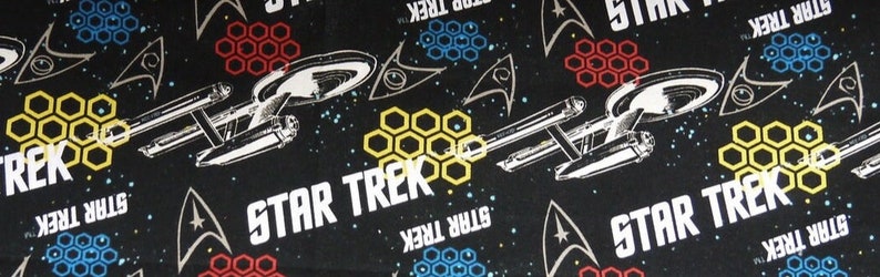 K&ouml;nnte beinhalten: Schwarzer Stoff mit einem sich wiederholenden Muster aus dem Star Trek-Logo, Sternen und Wabenformen in Gelb, Rot und Blau.