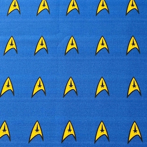 Pode incluir: Um tecido azul com um padrão repetido de insígnias amarelas da Starfleet.