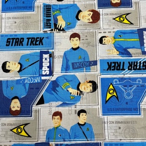 Può includere: Un tessuto blu e bianco con un motivo ripetuto di personaggi di Star Trek e il testo "Star Trek". I personaggi includono Spock, McCoy e Kirk. Il tessuto presenta anche il logo di Star Trek e il testo "U.S.S. Enterprise NCC-1701".