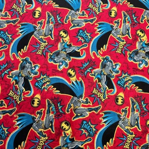 Puede incluir: Tela roja con un patrón repetido de un superhéroe con un traje negro y azul con un símbolo de murciélago amarillo. El superhéroe está pateando y tiene una capa. El fondo es rojo con estrellas amarillas y texto blanco que dice "KA-BOOM", "CRASHHH", "THACK" y "WHHS".