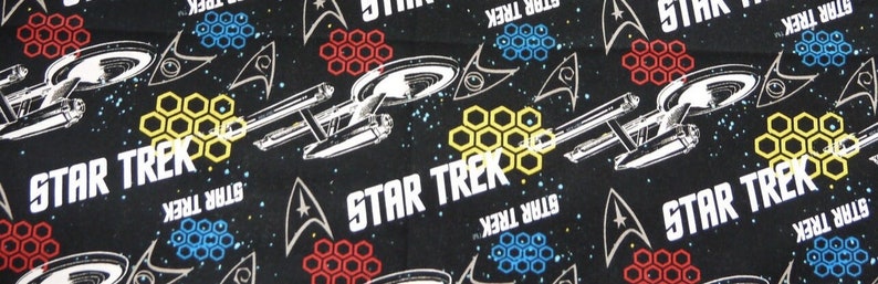 K&ouml;nnte beinhalten: Schwarzer Stoff mit einem sich wiederholenden Muster aus wei&szlig;en Raumschiffen, wei&szlig;em Text mit der Aufschrift "STAR TREK" und gelben, roten und blauen Wabenformen.