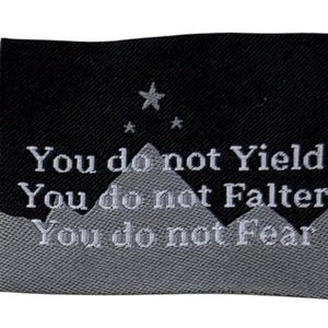 May include: Black and gray woven label with white text. The text reads "You do not Yield, You do not Falter, You do not Fear." A mountain range and stars are depicted above the text.