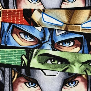 May include: Close-up of a fabric featuring comic book superhero faces. The design includes the eyes of characters like Thor, Iron Man, Captain America, and the Hulk. The colors are vibrant, with blue, green, red, and gold accents.